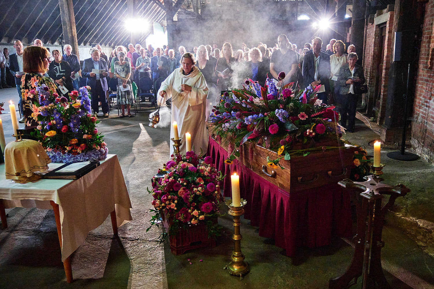 Foto van een katholiek afscheidsritueel tijdens een uitvaart. De priester gaat met wierook rondom de kist.