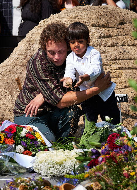 Kindje strooit zand op het graf tijdens het afscheid van zijn vader.